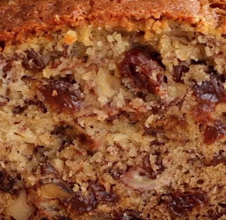 Moist banana bread topped with sliced bananas and walnuts on a wooden table.