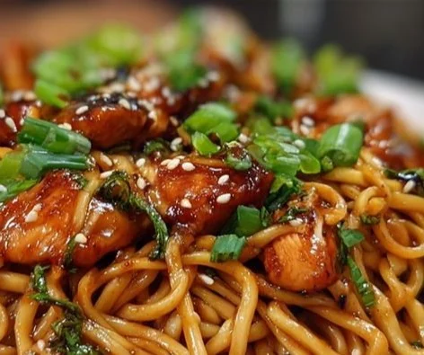 Plate of sticky garlic chicken noodles garnished with green onions
